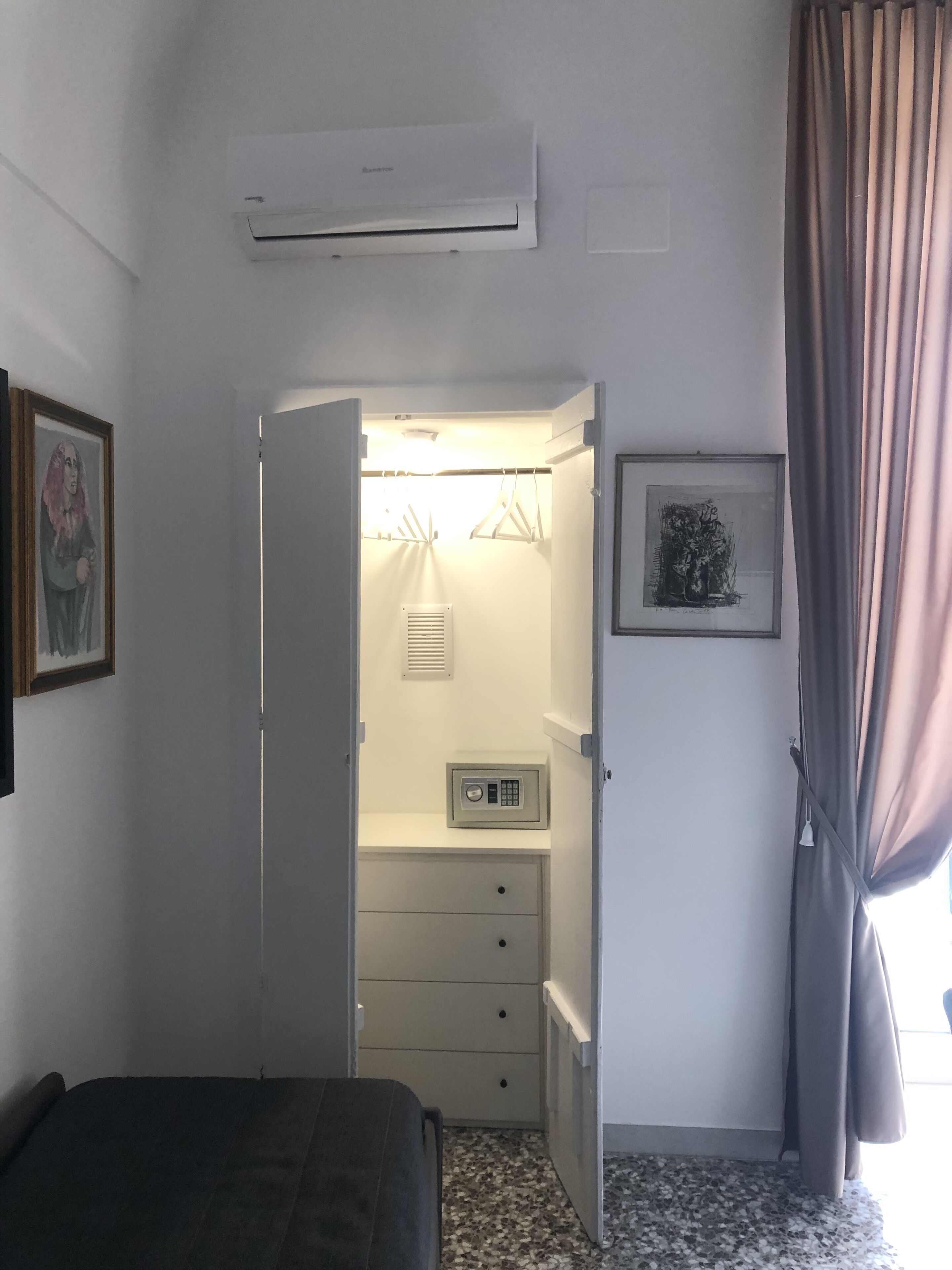 A bedroom with a bed, a wardrobe, a safe, and a framed picture on the wall.