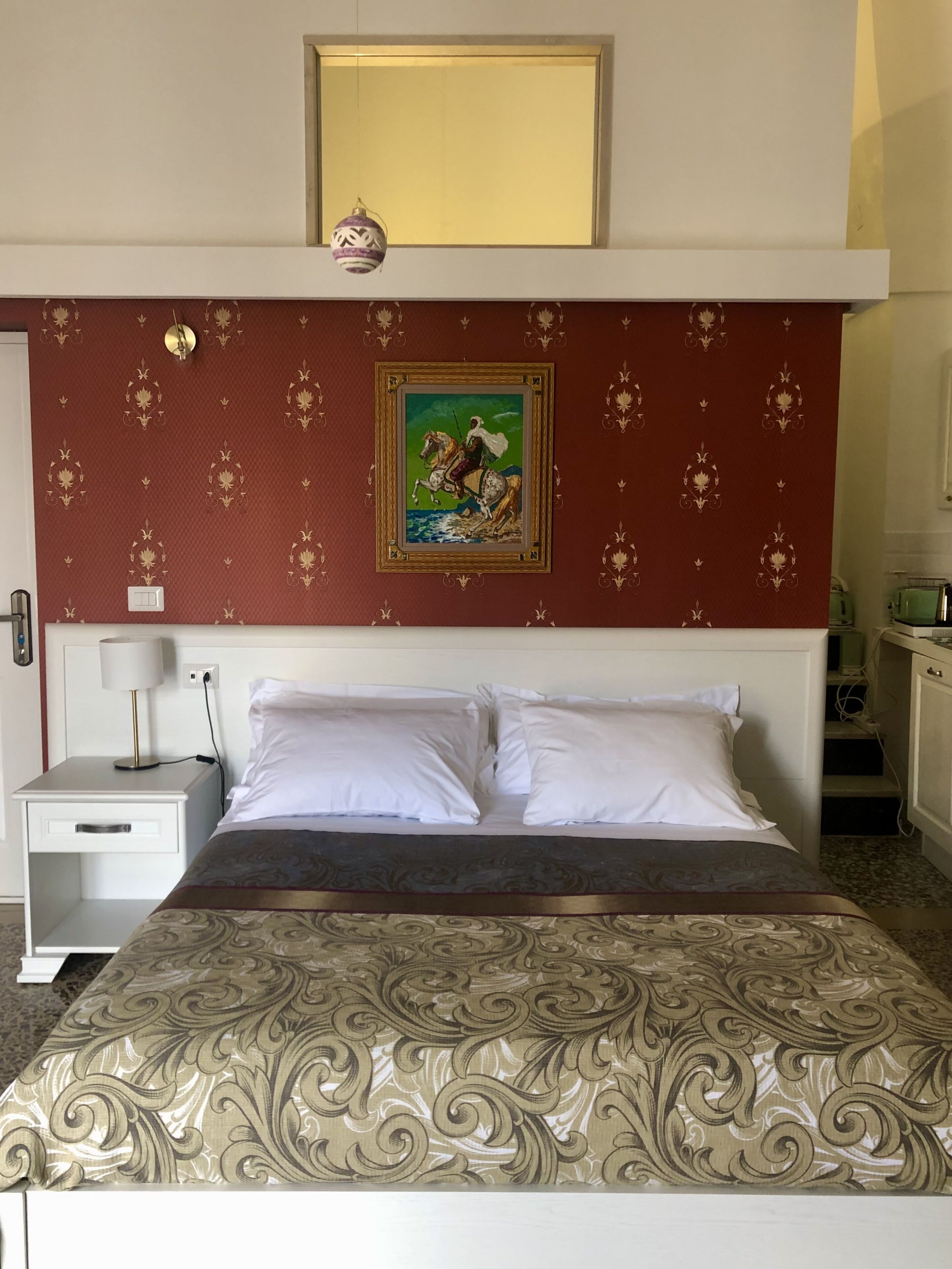 A hotel room with a bed, a nightstand, a lamp, a painting on the wall, and a small decorative item.