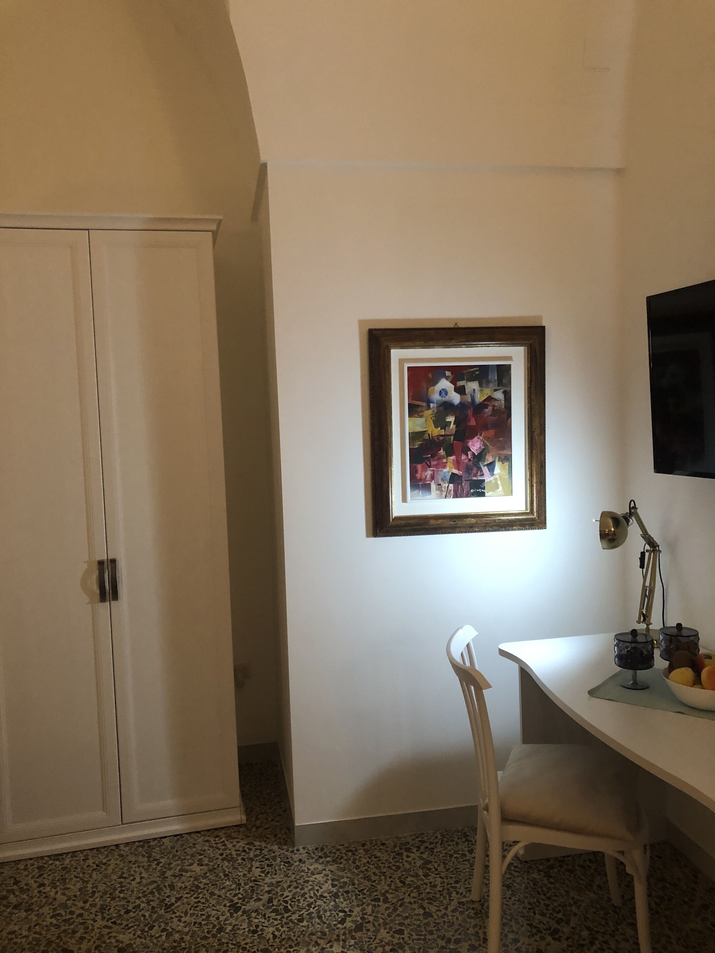 Una habitación con un escritorio blanco, un cuadro en la pared, una silla y un armario.