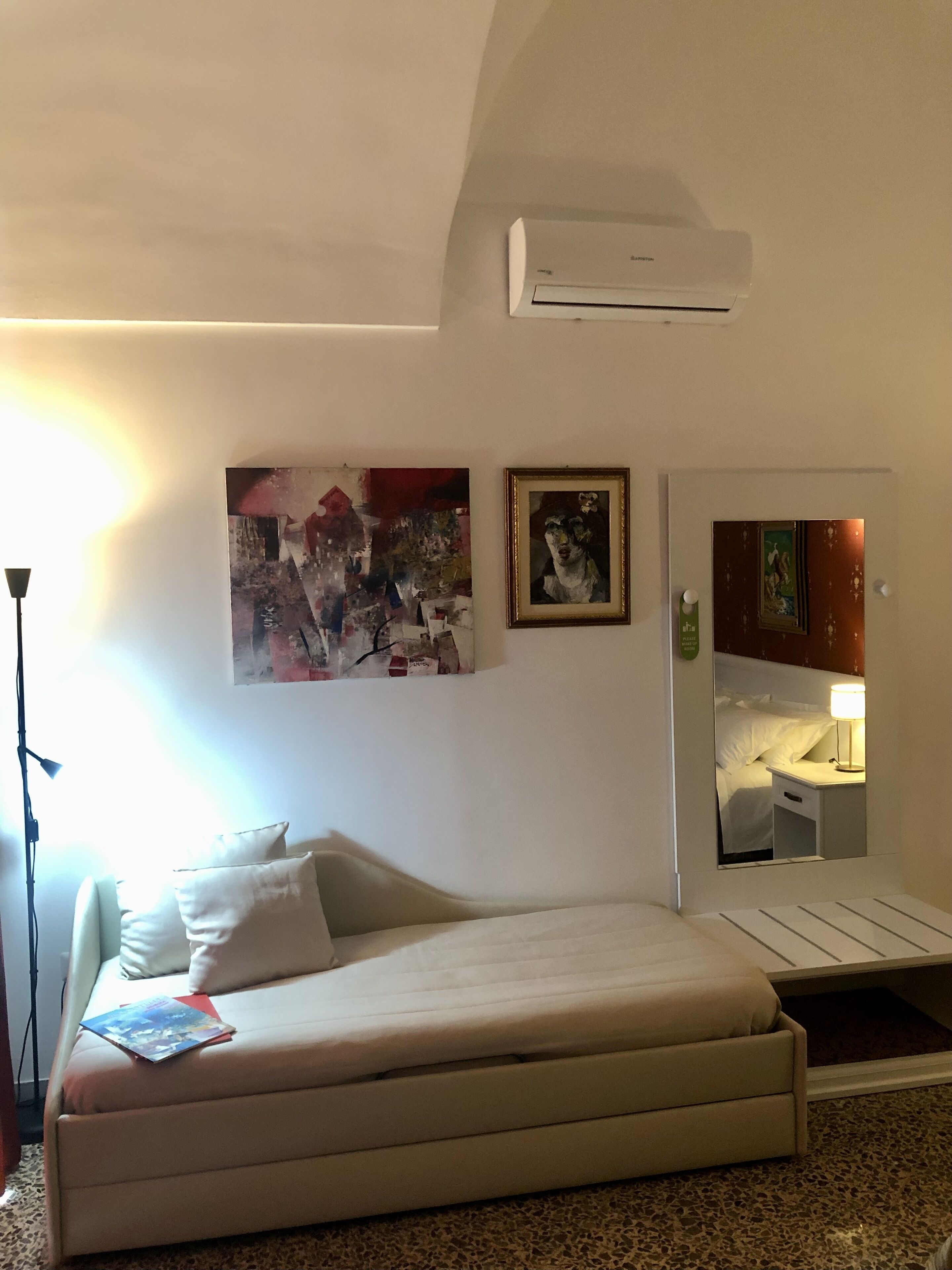 Una habitación de hotel con una cama, un aire acondicionado de pared y dos obras de arte enmarcadas.