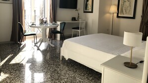 Et hotelværelse med seng, skrivebord, stole, fjernsyn og kunst på væggene.