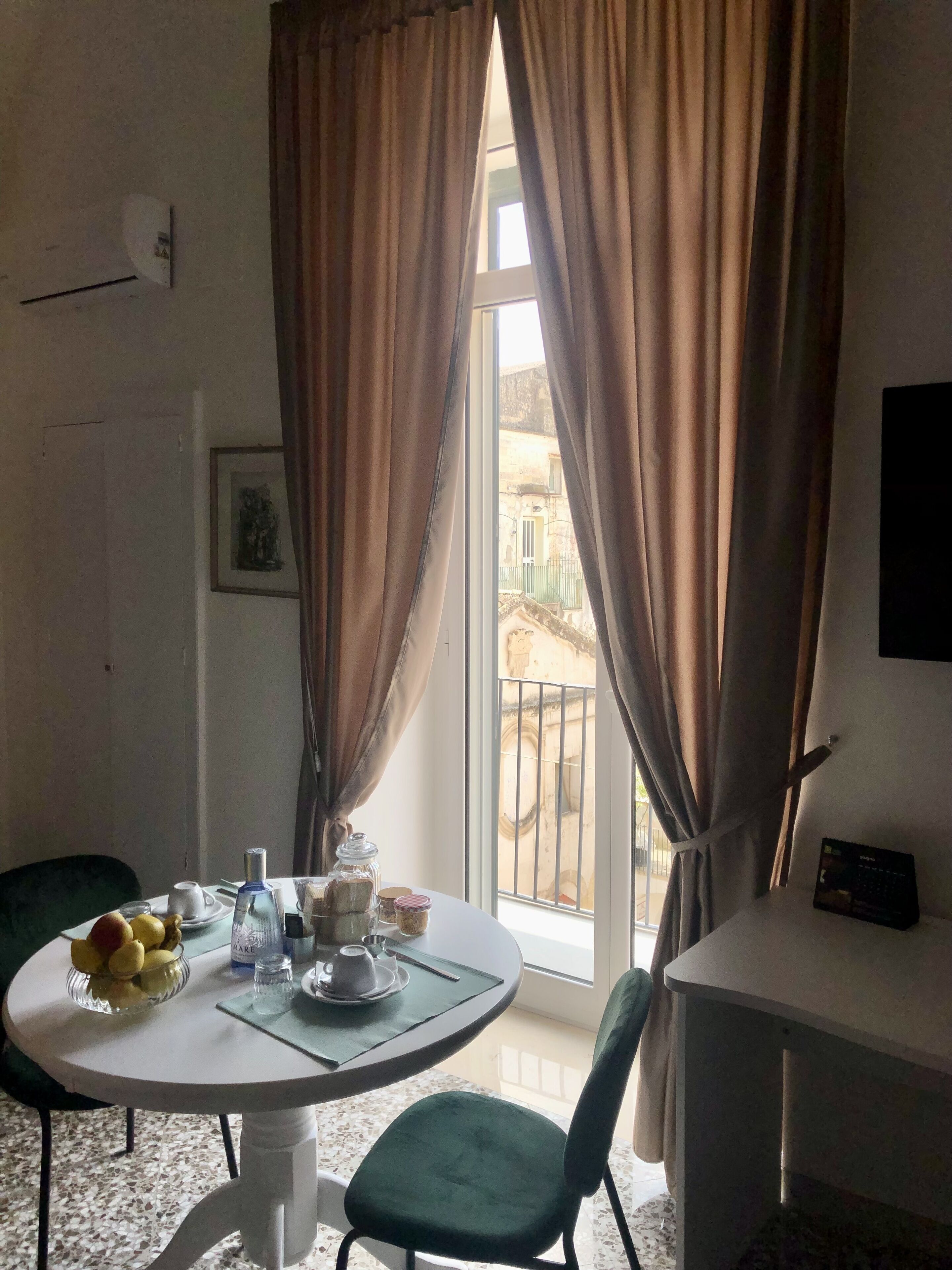 Una habitación con una mesa redonda para comer, una silla, un armario pequeño y una ventana con cortinas.