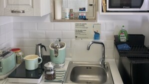 Et lille køkken med hvide skabe, en stålvask, en mikrobølgeovn og diverse køkkenapparater.