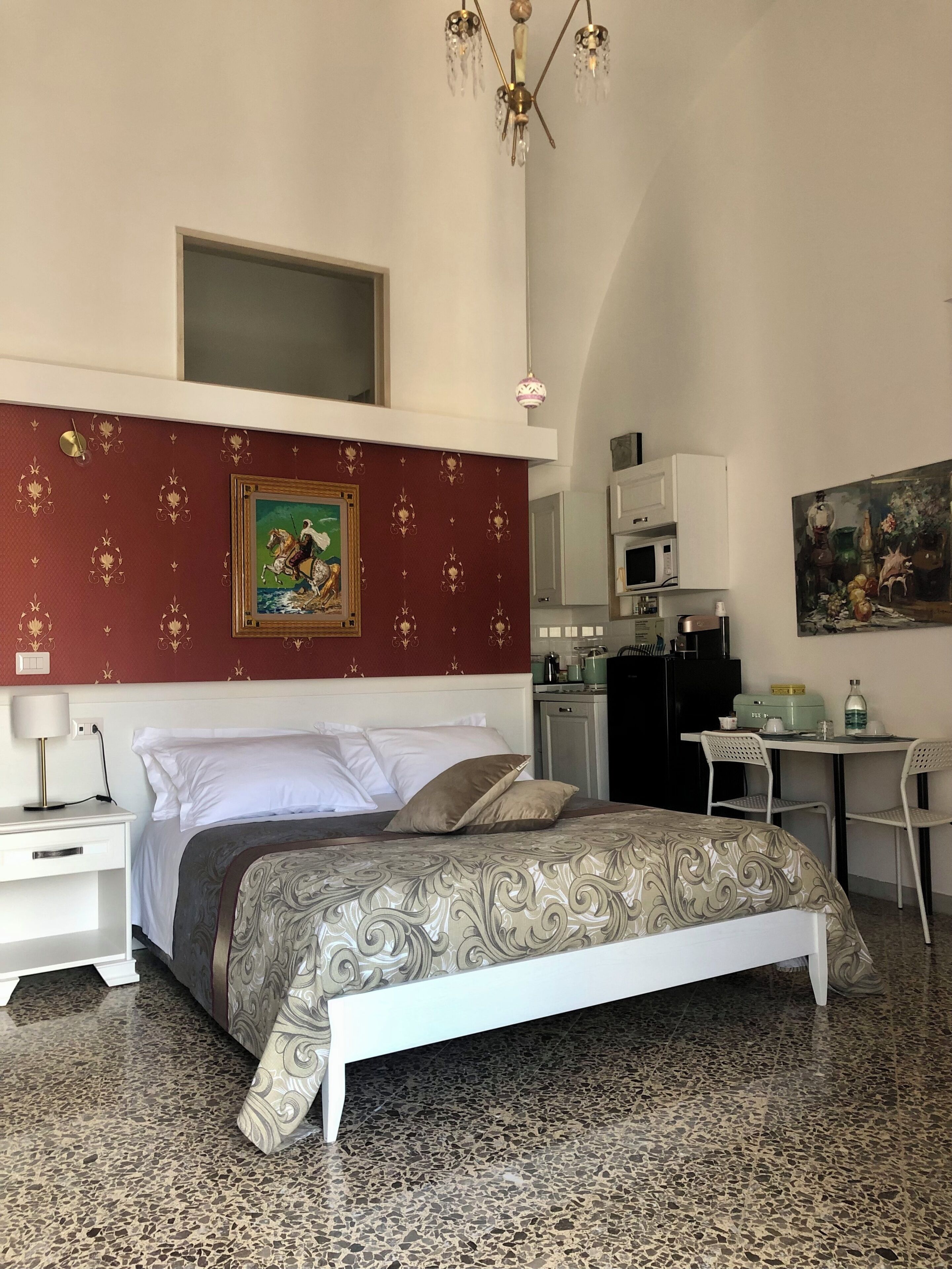 A bedroom with a bed, a desk, a chair, a microwave, and a painting on the wall.