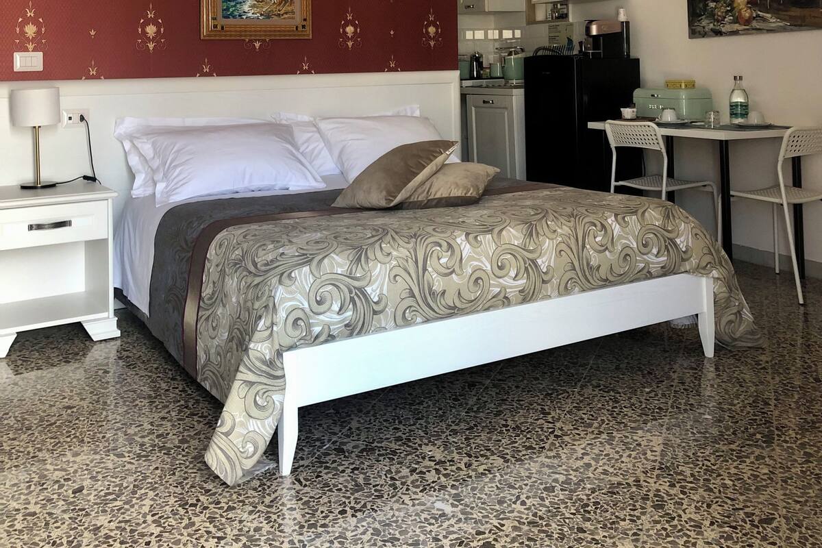 A bedroom with a bed, a desk, a chair, a microwave, and a painting on the wall.