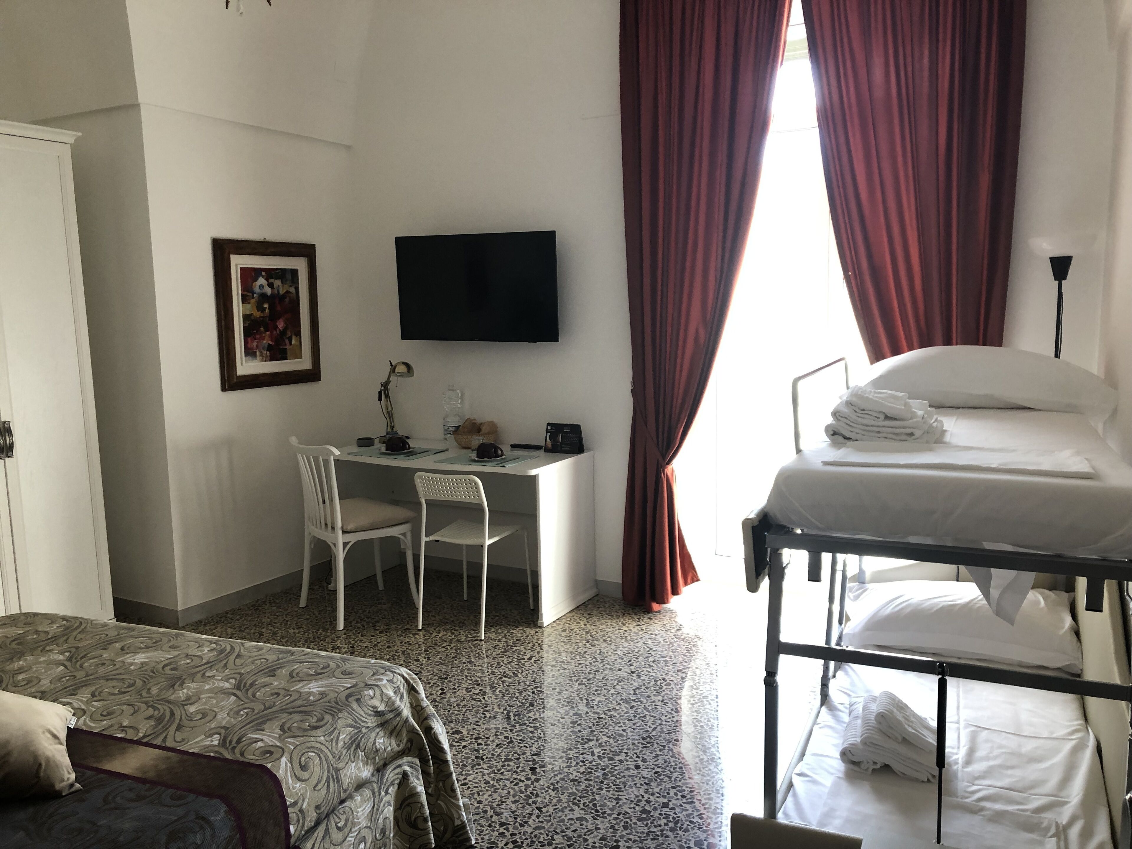 A hotel room with a bed, a desk with a chair, a TV, and a window with curtains.