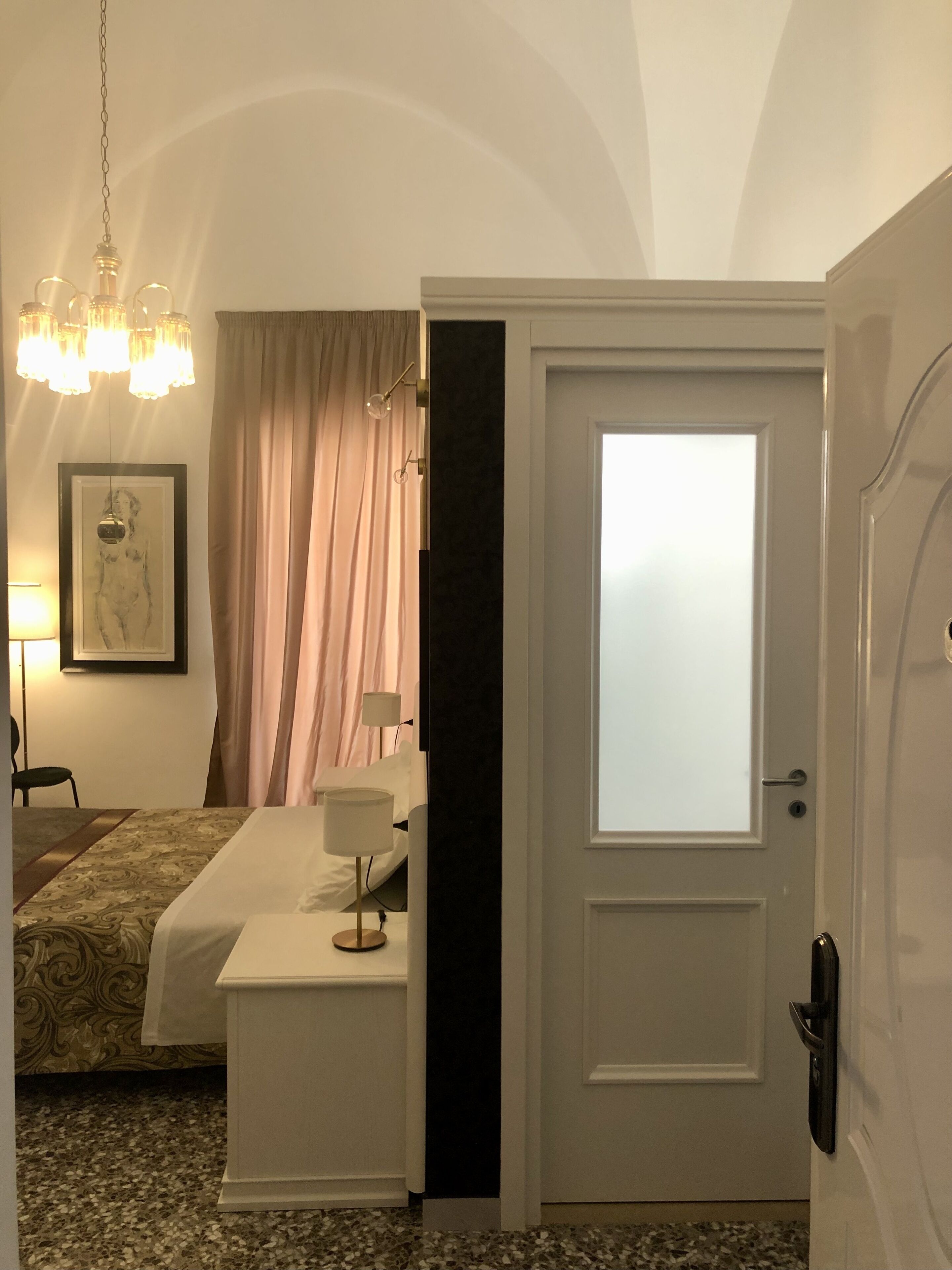 A hotel room with a bed, a desk, a chair, a lamp, a painting, and a door.