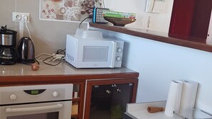 Eine kompakte Küche mit Backofen, Mikrowelle, Kaffeemaschine und kleinem Kühlschrank.