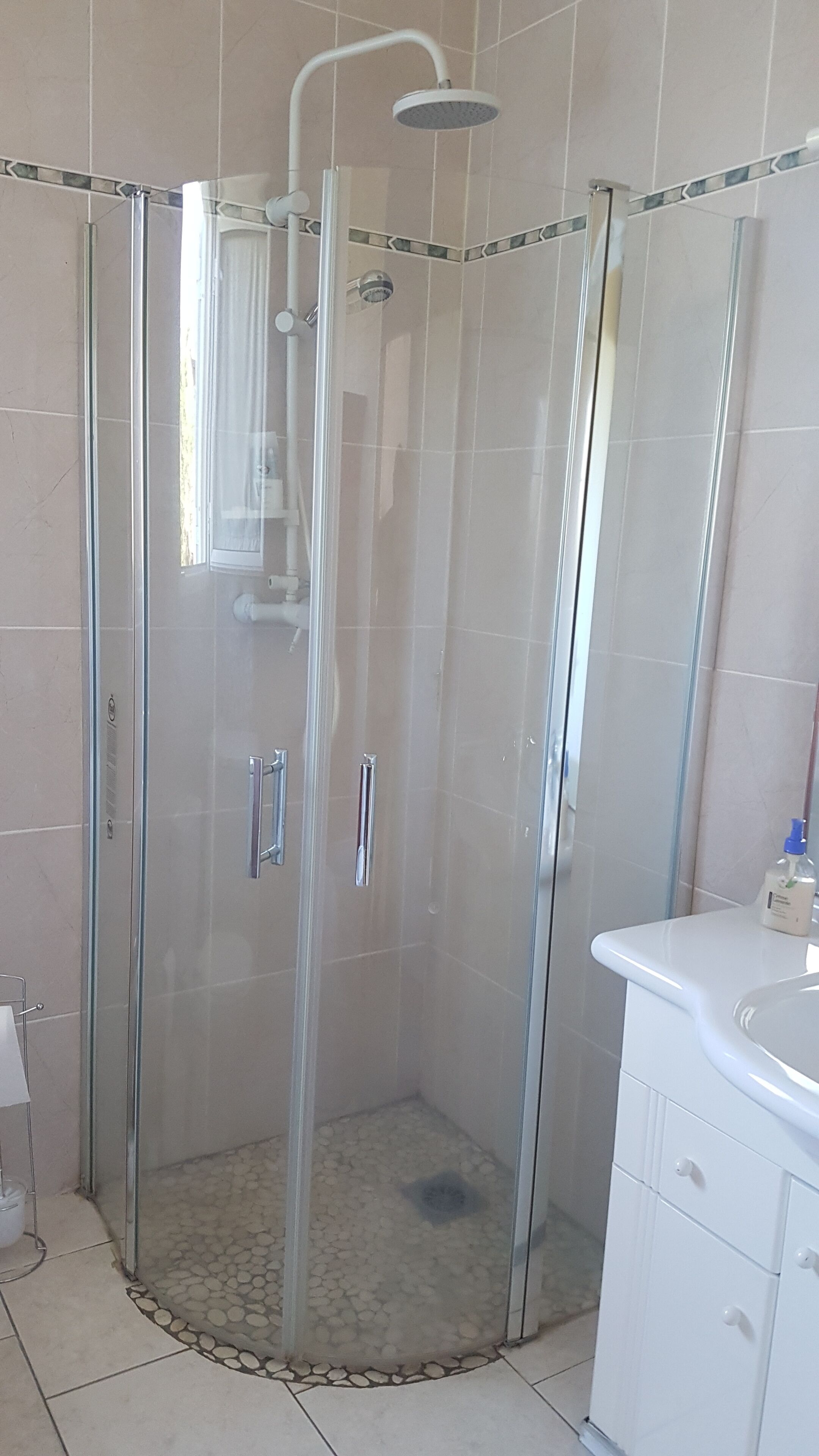 A glass-enclosed shower with a handheld showerhead, a tiled floor, and a white sink with a mirror.
