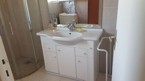 A bathroom with a white sink, two faucets, and a mirror. There is a shower area with a glass door and a tiled floor.