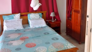 Ein Schlafzimmer mit einem Bett, einem Nachttisch, einem Holzschrank und roten Vorhängen.