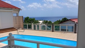 Ein Schwimmbad mit Meerblick, ein überdachter Bereich mit rotem Dach und eine Treppe, die zu einer höheren Ebene führt.