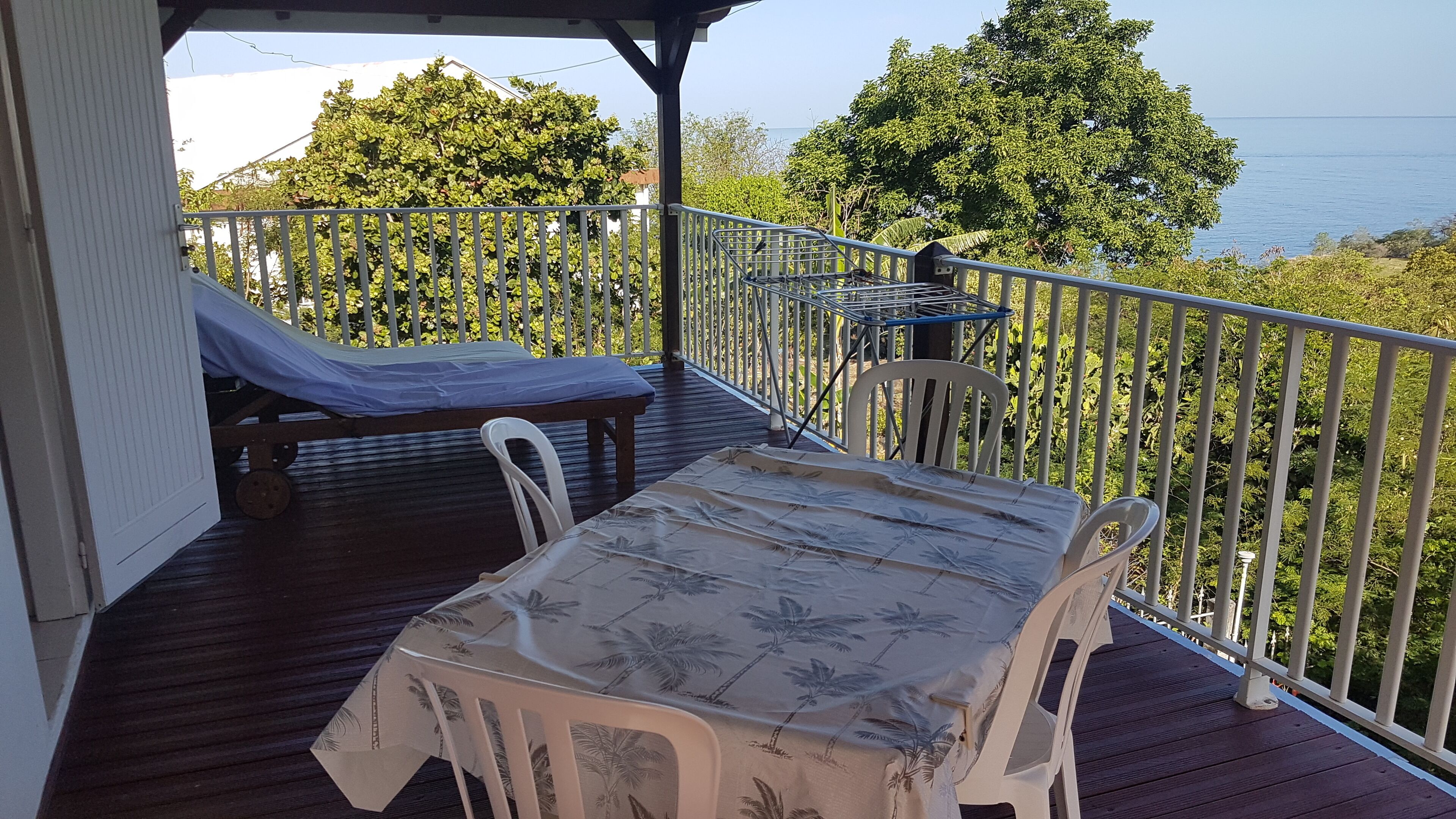 A covered outdoor deck with a table and chairs, a bench, and a view of the sea.