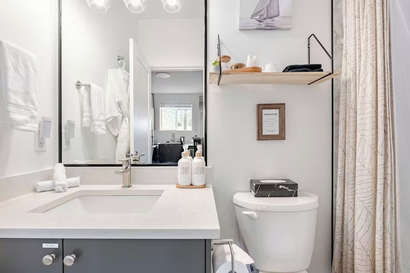 A modern bathroom with a large mirror, a sink, a toilet, and a shelf with toiletries.