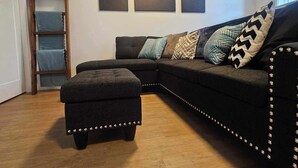 Un salon comprenant un canapé d’angle aux couleurs sombres, un pouf assorti et trois tableaux abstraits accrochés au mur.