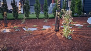 Un jardin aménagé avec des jardinières décoratives, un sentier en pierre et, au fond, un bâtiment dont la façade est en pierre.