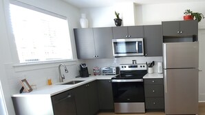 Une cuisine moderne avec des meubles gris, un réfrigérateur en acier inoxydable, un four à micro-ondes, une cuisinière et un évier.