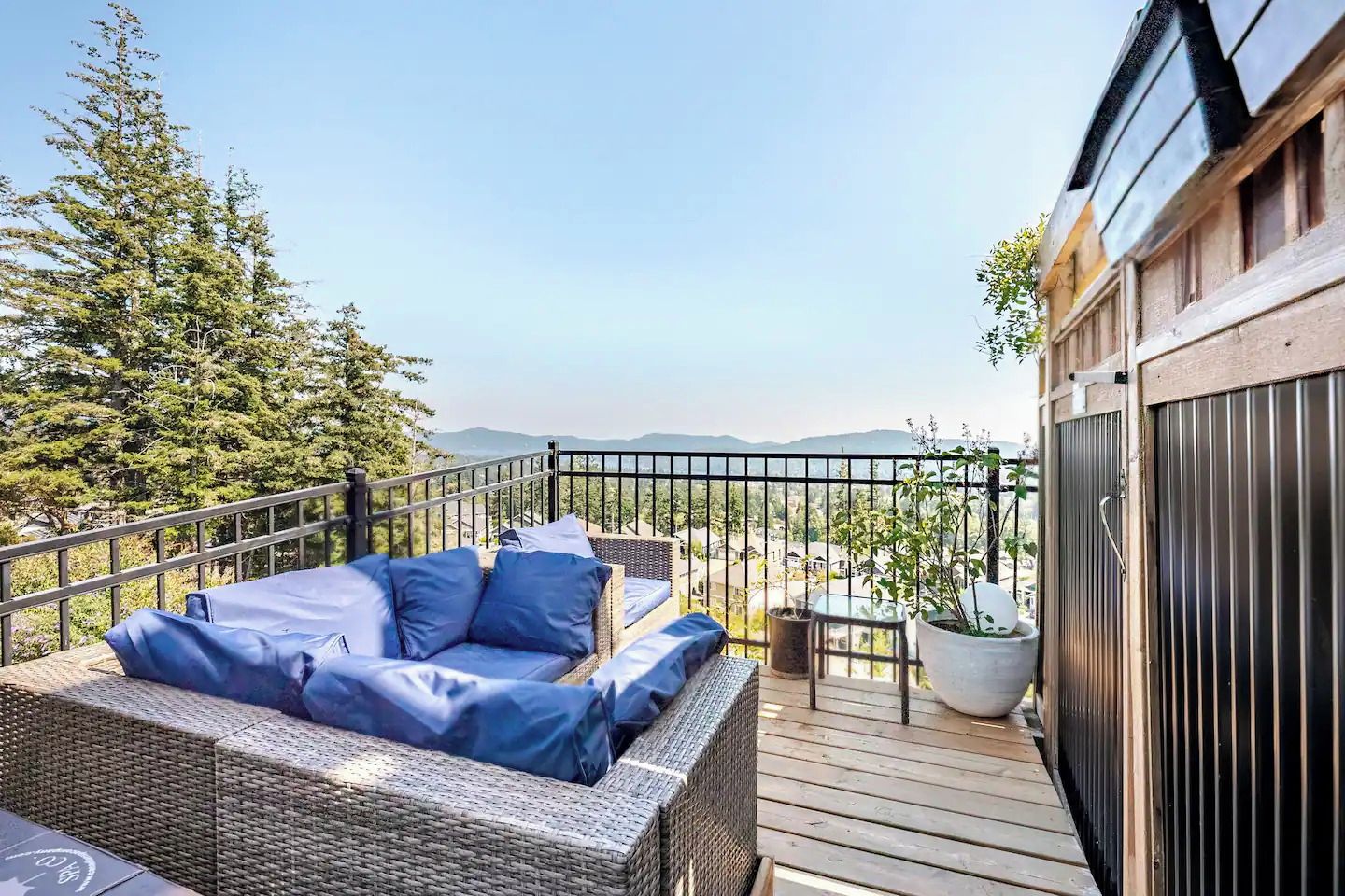 Un balcon agrémenté d’un canapé en osier, de plantes en pot et offrant une vue sur le paysage.