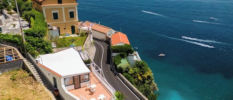 Ein Küstengebäude mit einer sich schlängelnden Straße zum Meer, einem Balkon mit Gartenmöbeln und Blick auf den Ozean.