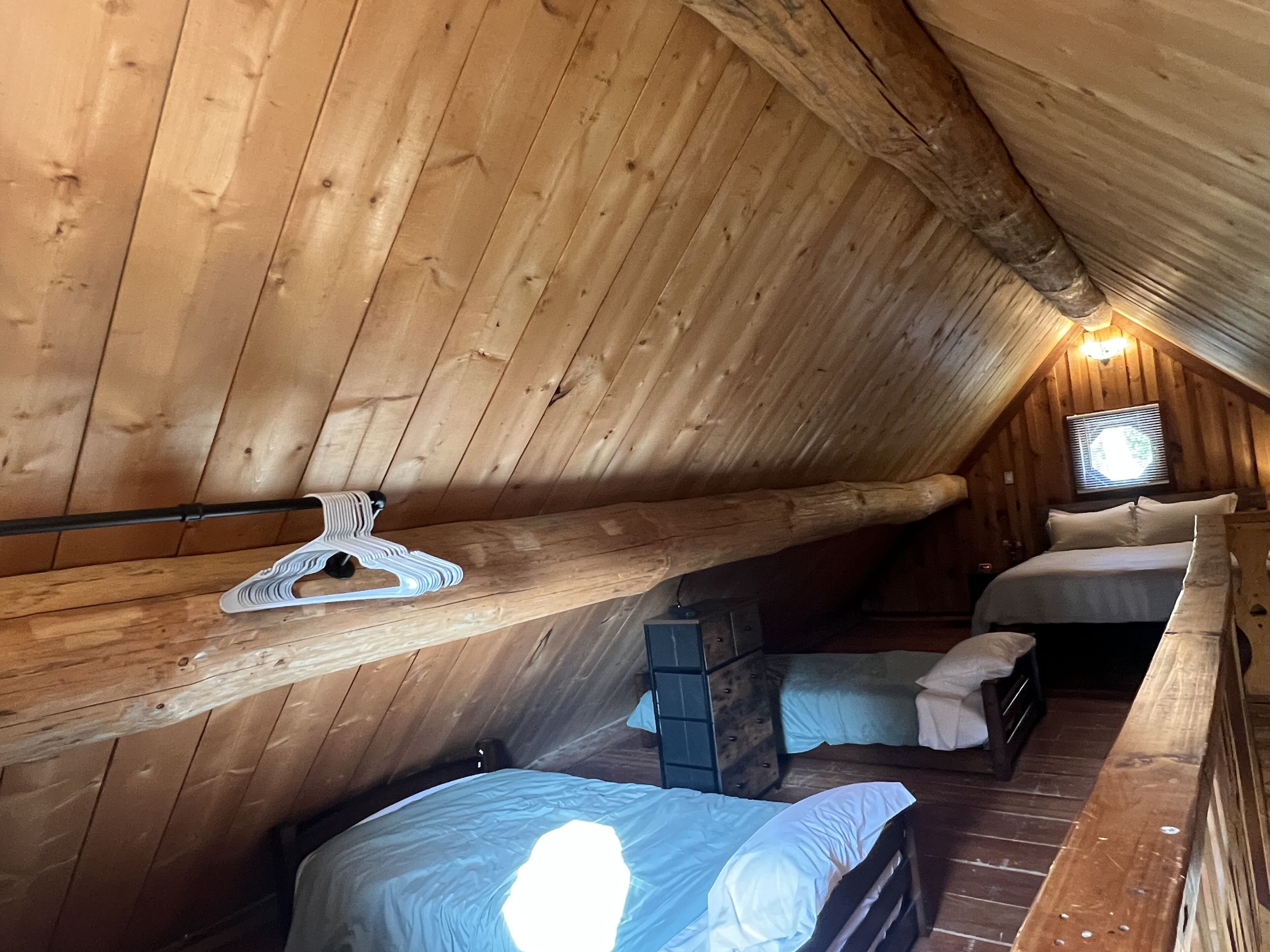 Un dormitorio acogedor en el ático con paredes de madera, techo inclinado, cama, banco y perchero.