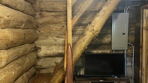 Una scala in legno all'interno di una baita di tronchi, con un televisore su un mobile in legno.