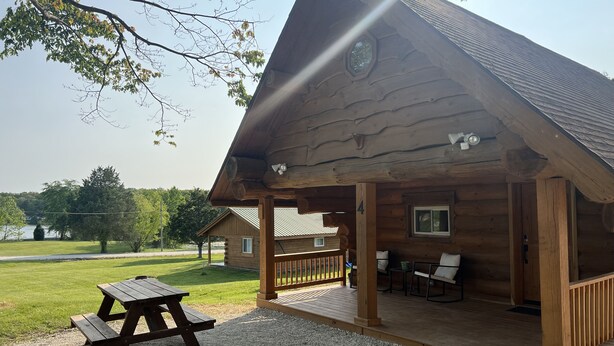 Una baita di legno con veranda coperta, tavolo da picnic e vista su un lago.