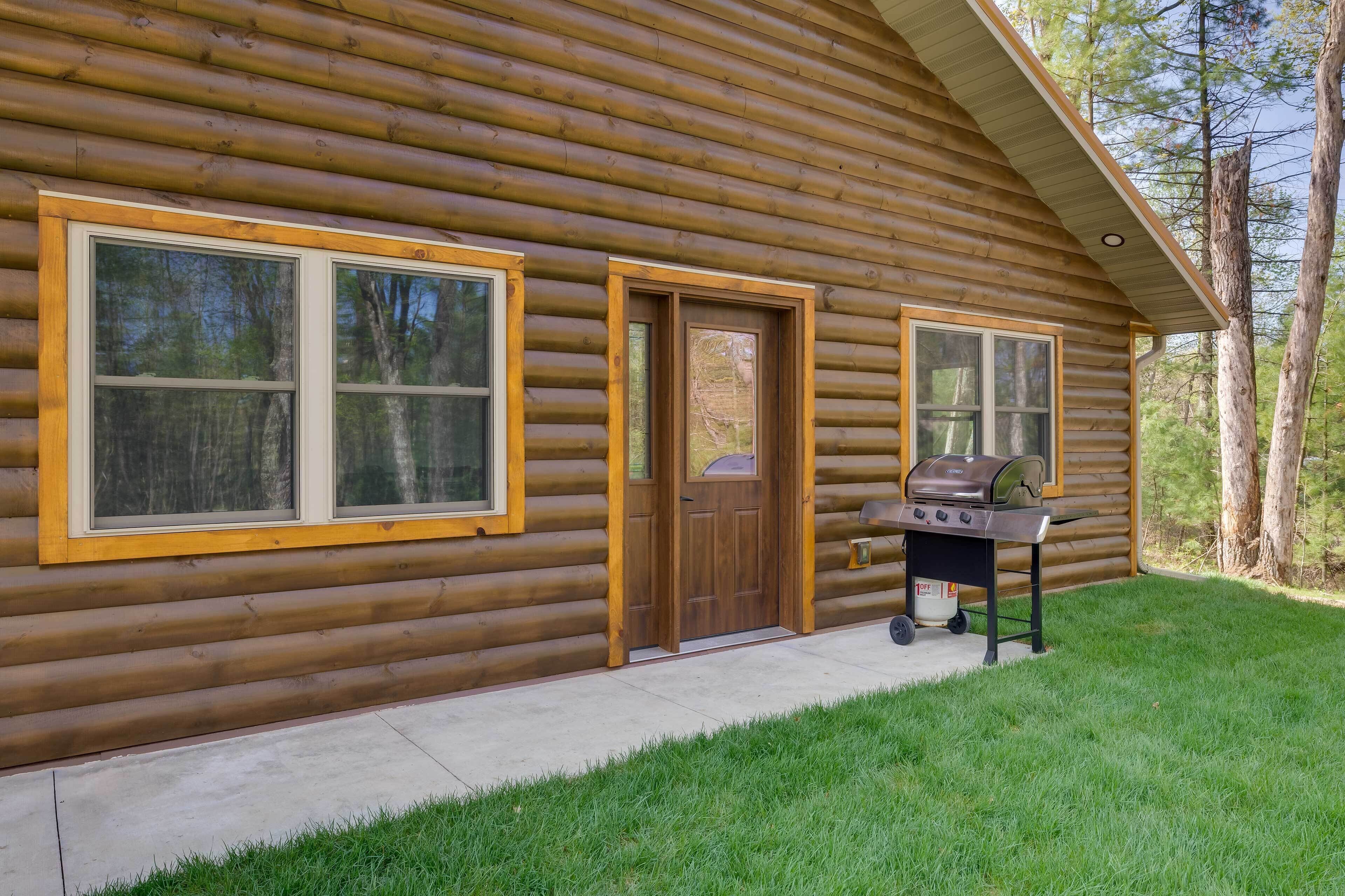 A log cabin with a front door, two windows, and a grill outside.