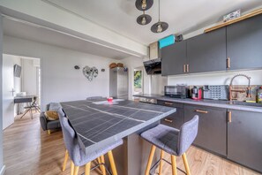 A modern kitchen with dark cabinets, a large island with stools, and a dining area with a table and chairs.