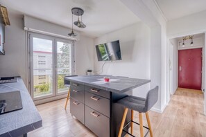 A modern kitchen with a large island, a dining area with a bar stool, and a TV mounted on the wall.