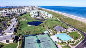 An aerial view of a coastal resort with multiple buildings, a tennis court, and a beach. - Ocean Village South Floridas Premier Gated Ocean Front Resort with Pool and Golf (Hutchinson Island)