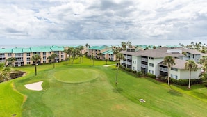 A golf course with a putting green, surrounded by multi-story buildings with green roofs and palm trees. - Ocean Village South Floridas Premier Gated Ocean Front Resort with Pool and Golf (Hutchinson Island)