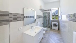 A modern bathroom with a shower, toilet, and washing machine. - Agave House (Forio)