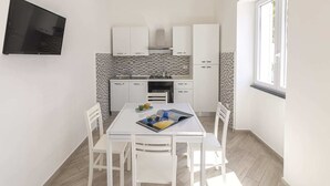 A compact kitchen with white cabinets, a tiled backsplash, and a dining area with a table and chairs. - Agave House (Forio)