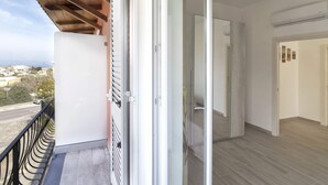 A balcony with a view of a road and buildings, an open door leading to a room with a wooden floor, and a white wall with a picture frame. - Agave House (Forio)