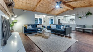 A spacious living room with a high ceiling, built-in wooden beams, and a modern kitchen in the background. - Heated Pool, Putting Green, Movie Theater and more! 4 bed/3 bath (Dallas)
