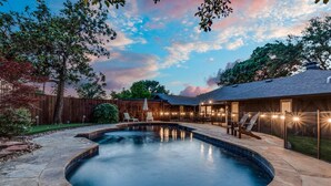 A backyard with a swimming pool, stone patio, wooden fence, and outdoor seating area. - Heated Pool, Putting Green, Movie Theater and more! 4 bed/3 bath (Dallas)