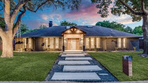 A two-story brick building with a central entrance, a covered porch, and a gravel pathway leading to the door. - Heated Pool, Putting Green, Movie Theater and more! 4 bed/3 bath (Dallas)