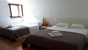 Ein Hotelzimmer mit zwei Einzelbetten, jeweils mit einer braunen Tagesdecke und weißen Kissen. Ein kleiner Nachttisch beherbergt eine Lampe und eine dekorative Vase. Der Raum verfügt über einen Holzboden und ein Fenster mit Holzrahmen.