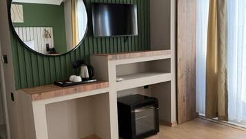 A room with a wooden desk, a black trash bin, a mounted TV, and a large mirror.