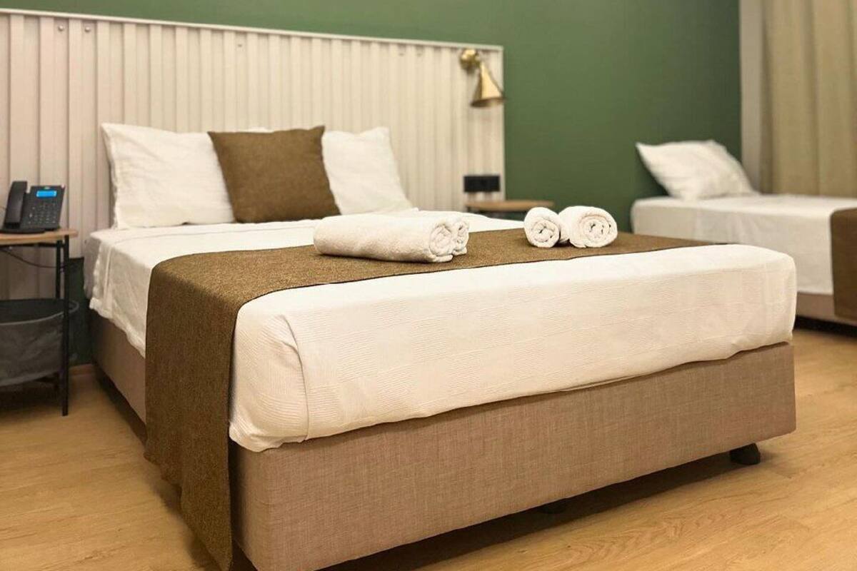 A hotel room with a large bed, a smaller bed, and a sofa. There is a telephone on a side table.
