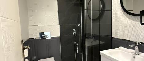 Une salle de bain moderne avec une douche à parois de verre, des toilettes blanches et un lavabo blanc avec un miroir au-dessus.