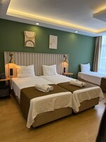 Habitación de hotel con dos camas, una mesita de noche con lámpara, un reloj de pared y una cita enmarcada.