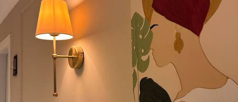 Un mur orné d’un tableau représentant le profil d’une femme et une lampe fixée au mur.