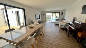 A spacious living area with a wooden dining table, modern chairs, a piano, and a TV. - Villa Climatiséeavec Piscine Chauffee, Proche mer (Angoulins)