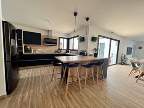 Una cocina moderna con una isla central, taburetes de bar y una zona de comedor con sillas.