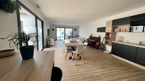A modern living room with a dining area, a piano, and a view of a pool through large glass doors. - Villa Climatiséeavec Piscine Chauffee, Proche mer (Angoulins)