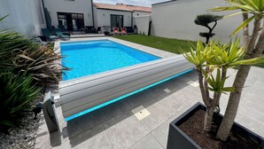 A modern outdoor pool area with a wooden deck, surrounded by potted plants and a well-maintained lawn. - Villa Climatiséeavec Piscine Chauffee, Proche mer (Angoulins)
