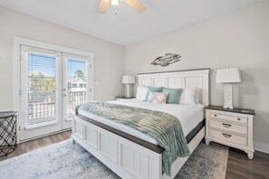 A bedroom with a large bed, two bedside tables, a window with blinds, and a view of the outside.