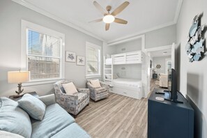 Une chambre à coucher de taille modeste, équipée d’un lit superposé, d’un ventilateur de plafond et d’un téléviseur posé sur une commode.