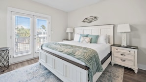 Quarto com cama grande, duas mesas de cabeceira, janela com persianas e vista para o exterior.